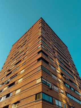 Geometrik çizgileri, klimaları ve pencereleri olan, şehir mimarisi kavramları için ideal, canlı mavi gökyüzüne karşı kurulmuş, yüksek tuğlalı bir apartmanın yukarı manzarası..