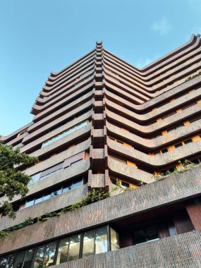 Benzersiz kıvrımlı balkonları, yemyeşil ve berrak mavi gökyüzü olan çağdaş tuğla gökdelenlerin çarpıcı perspektifi mimari ve şehir manzarası kavramları için idealdir..