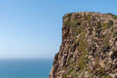 Sade bitki örtüsüyle sarp kayalıklar berrak bir gökyüzü altında mavi Atlantik Okyanusu 'nun üzerinde yükseliyor Lizbon bölgesinin vahşi sahil güzelliğini seyahat ve doğa esin kaynağı olarak yakalıyor..