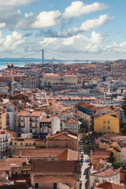 Geleneksel kırmızı çatılar, tarihi mimari ve dramatik gökyüzü altındaki ünlü 25 de Abril Köprüsü 'nün yer aldığı canlı Lizbon şehir manzarası seyahat ve kentsel ilham için mükemmel..