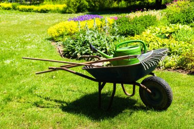 Gardener s wheelbarrow with the gardening tools in the gardens with flower beds in the background. Gardening concept