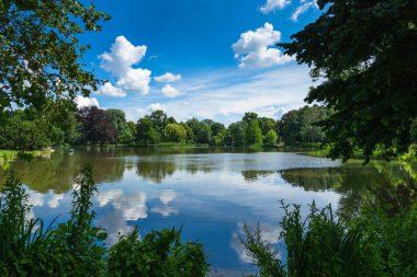 Unique panoramic skyline view of Masch Park and lake, New Town Hall, Hannover, Germany. Luscious green trees foliage and summer blue sky reflections in serene lake waters.