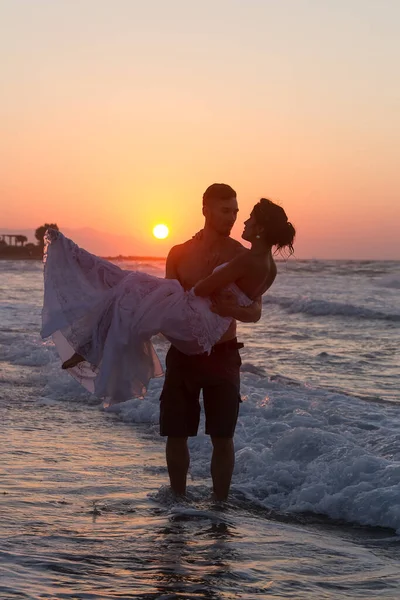 在夏末的暮色中 新婚夫妇穿着婚纱和短裤 赤脚散步 浑身湿透 互相取笑和亲吻 在海滩上完婚 — 图库照片
