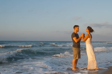 Genç bir adam ve genç bir kadın, el ele tutuşan sevgi dolu genç bir çift ıslak kumda çıplak ayakla yürümekten, yaz akşamında romantizmden zevk alırlar. Seyahat yaşam tarzı konsepti.