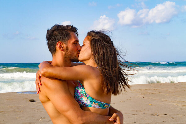 Young couple embracing and kissing at the beach in summer at dusk