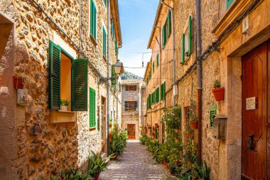 Taş döşeli dar sokaklar, seramik kaplarda bitkiler, taş evler, ahşap yeşil pencereler, Valdemossa ortaçağ köyü, Mallorca, Balear Adaları, İspanya.