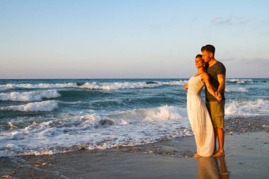 Genç bir adam ve genç bir kadın, sevgi dolu genç bir çift ıslak kumda çıplak ayakla yürümeyi, yaz akşamında romantizm yapmayı severler. Seyahat yaşam tarzı konsepti.