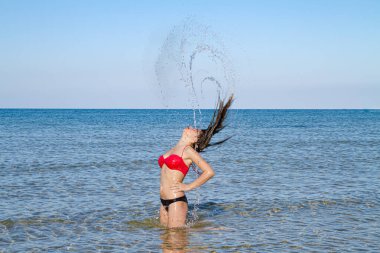 Yumuşak tenli, narin vücutlu mutlu stressiz bikinili kadın, deniz suyu sıçratarak eğleniyor, temiz hava soluyor yaz tatilinin tadını çıkarıyor.