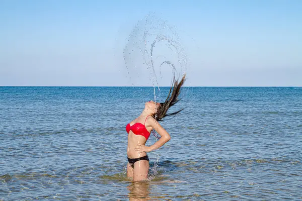Yumuşak tenli, narin vücutlu mutlu stressiz bikinili kadın, deniz suyu sıçratarak eğleniyor, temiz hava soluyor yaz tatilinin tadını çıkarıyor.