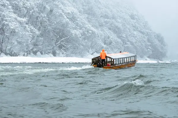 Winter Boat Journey on the Mogami River, Yamagata A traditional wooden boat navigates the cold waters of the Mogami River surrounded by snow-covered forests in Yamagata, Japan.