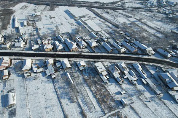 Aerial view of snow-covered family houses and surrounding areas near the road. Countryside.