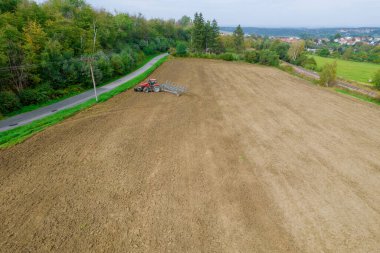 Tractor with a plow turns on a plowed field. Field road and forest near the field. View from above.