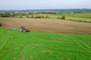 The tractor is plowing the land sown with green manure near the railway in the countryside. Soil preparation for sowing. View from above.