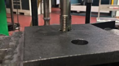 Close-up video of tapping a pre-drilled hole on a radial drilling machine in a workshop.