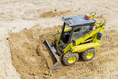 A mini tractor-loader moves and loads earth on a construction site. Leveling the surface of the land before construction.