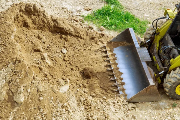 A mini tractor-loader moves and unloads earth on a construction site. Mini loader bucket, top view.