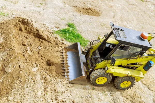 A mini tractor-loader moves and unloads earth on a construction site. Leveling the surface of the land before construction.