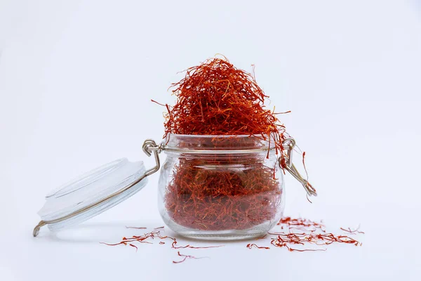 stock image An overflowing glass jar of dry saffron stamens on a white table. Dry spice, use in cooking and medicine.