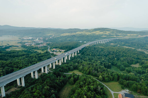 Транспортный мост в горной местности, дорога и деревья. Панорамный вид на природу сверху.