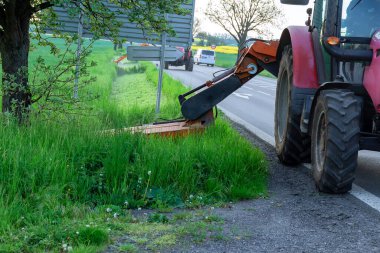 Döner çim biçme makineli bir traktör yol kenarında yeşil çim biçer. Kaldırımları temizlemek, yol kenarlarını biçmek....
