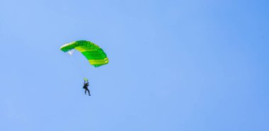 Açık yeşil paraşüt paraşütü olan bir paraşütçü mavi gökyüzü ve beyaz bulutların arka planına karşı. Paraşütle atlama.