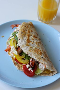 Yumurta tabanında karides, avokado, dolma biber ve ıspanakla dolu tortilla dürümü. Sağlıklı bir ev yemeğinin renkli ve protein dolu yan görüntüsü