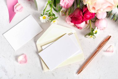 White card with envelop mockup on white marble table background with bunch of flowers, wedding stationery, event and greeting card