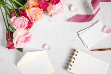 Wedding invitation and event planning background, notebook with card, envelop and gold pen with bunch of flowers on marble table, top view