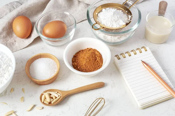 Baking pastry or cake ingredients, flour, brown sugar, milk, eggs on marble table with notebook and pen on marble table
