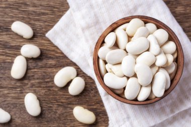 Tahta kasede beyaz fasulyeler, tahta masa arkasında çizgi üzerinde kumaş, üst manzara.