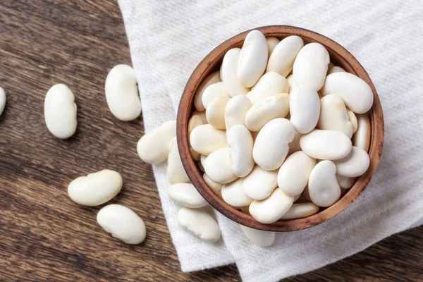 stock image White beans in wooden bowl on line cloth, top view