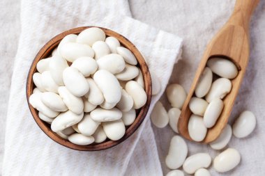 Ahşap kasede beyaz fasulye, keten kumaş arka planda kepçe, üst manzara.