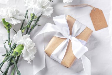 Beyaz yay ve çiçek arkaplanlı el sanatları kağıdına sarılı hediye kutusu, üst görünüm