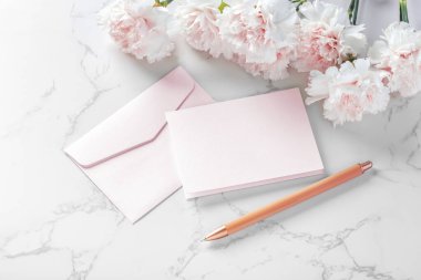 Mermer zemin üzerinde pembe çiçek ve kalem olan pembe kart ve zarf.
