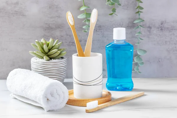 Dental care and dental hygiene concept, bamboo toothbrushes in cup with mouthwash and towel