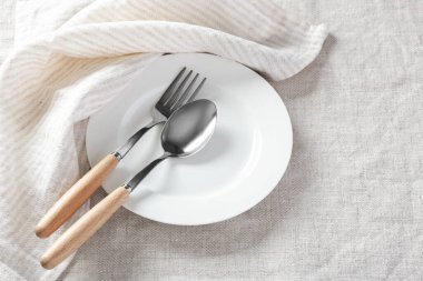 Beyaz tabak kaşıklı, çatallı ve peçeteli keten masa örtüsü.