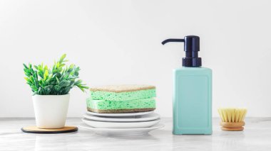 Yeşil bulaşık deterjanı ve beyaz mermer mutfak masasında fırça temizleme süngeri.