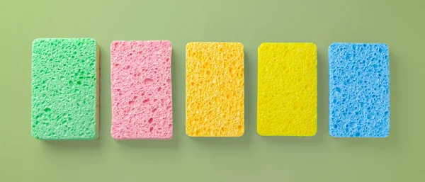 Colorful cleaning sponges on green background, top view