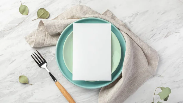 Wedding menu card mockup on plate with linen napkin on marble table, top view