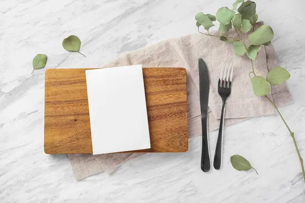 Wooden board and menu card mockup with fork and knife on marble kitchen table, top view