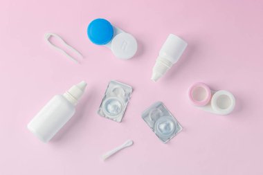 Konteynır, çözüm şişesi ve aksesuarlı kontak lensler pembe arka planda, üst görünümde
