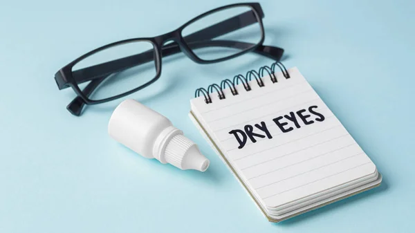 Eye drops and eyeglasses with dry eyes word on notebook on blue background