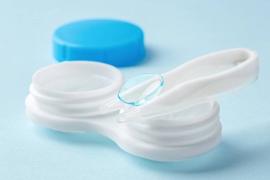 Açık mavi arkaplanda konteynırı olan cımbız üzerindeki kontak lensi, kapat