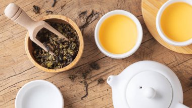 Çaydanlık ve çay fincanı ile ahşap masanın üstünde kurumuş çay yaprakları.