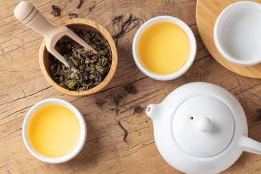 Tahta kasede çay yaprakları ve ahşap masada çaydanlık, üst manzara.