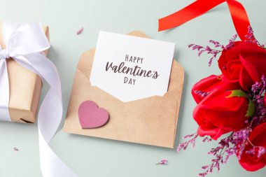 Kraft zarfındaki sevgililer günü kartında kalp, hediye kutusu ve pastel yeşil arka planda gül buketi var.