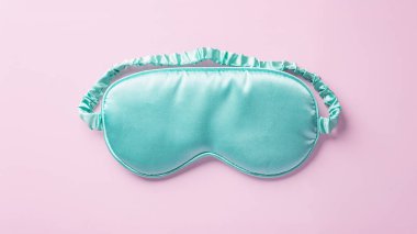 Turkuaz ipek uyku maskesi. Pastel pembe arka plan, üst manzara.