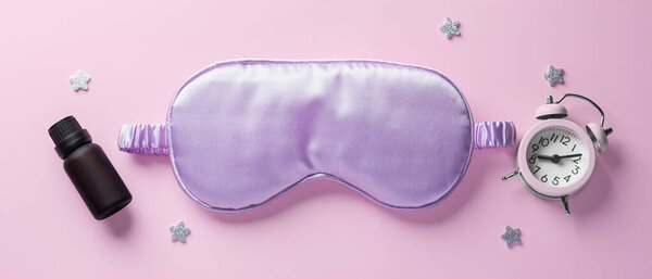 Purple sleep mask with alarm clock, essential oil, stars on pink background, top view