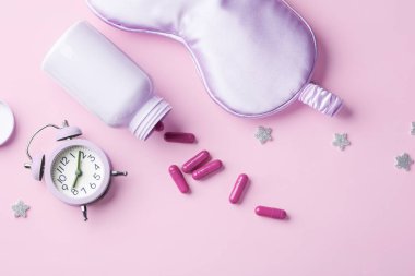 İlaç kapsülleri, uyku maskesi ve pastel pembe arka planda yıldızlar, uyku konsepti, düz yatak.