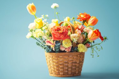 Kale sepetinde çiçekler turuncu lale ve mavi arka planda sarı güller.
